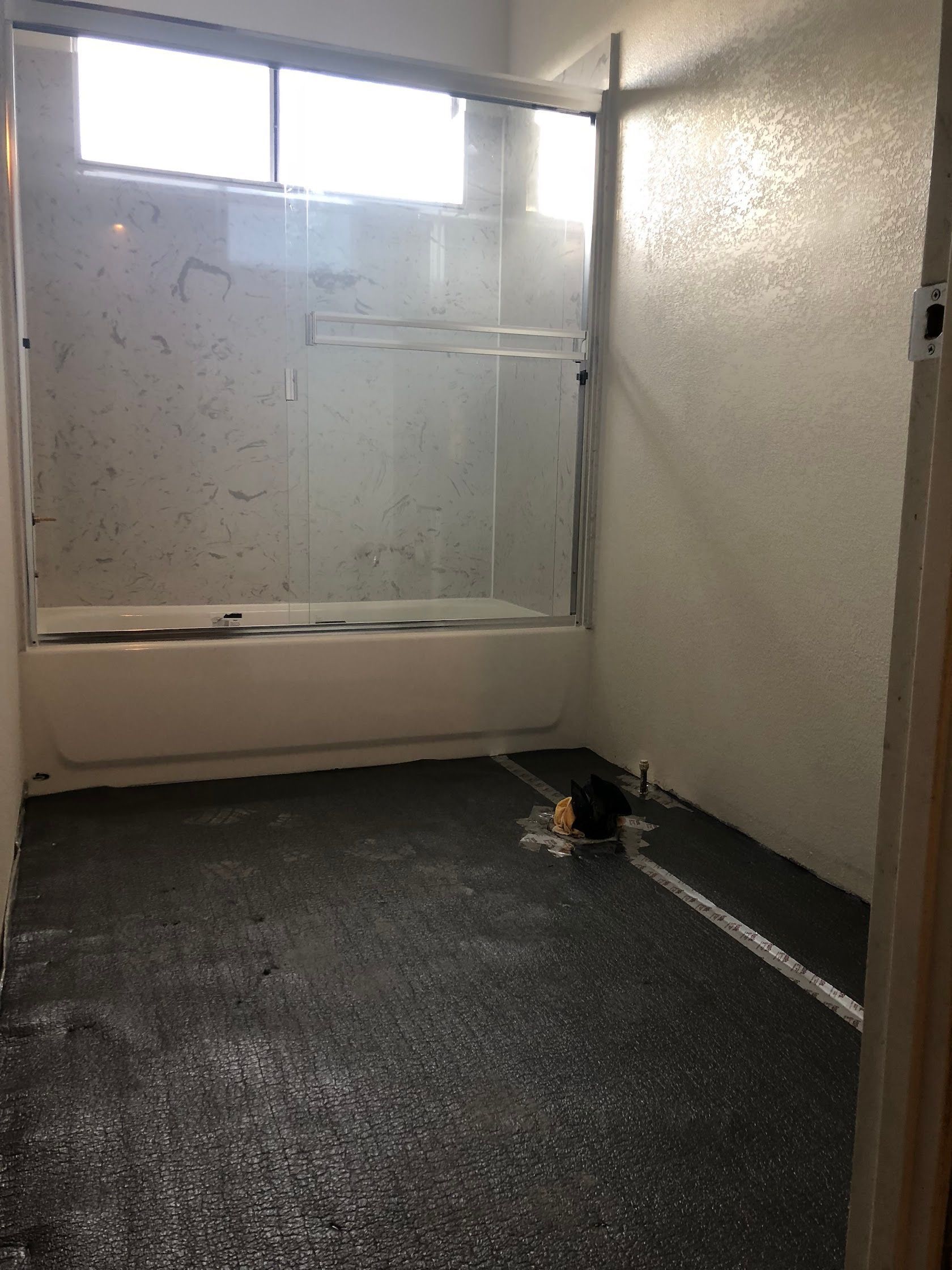 Small bathroom with tub, mirror, and wet dark floor in a bright, sparsely furnished room