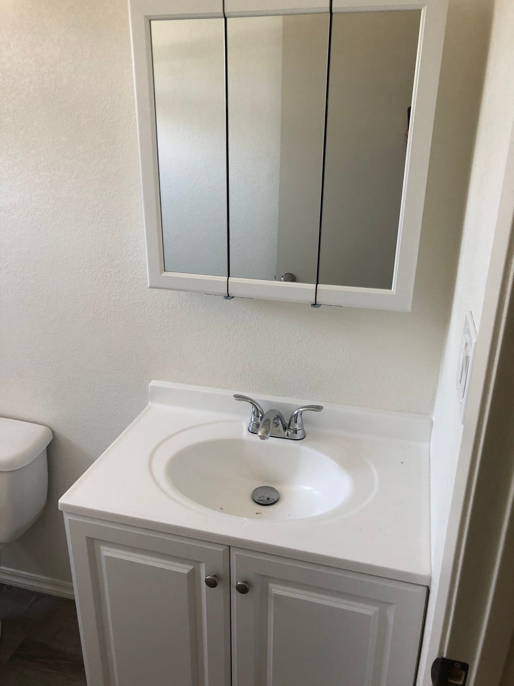 Small bathroom vanity with white sink, mirror cabinet, and toilet partially visible.