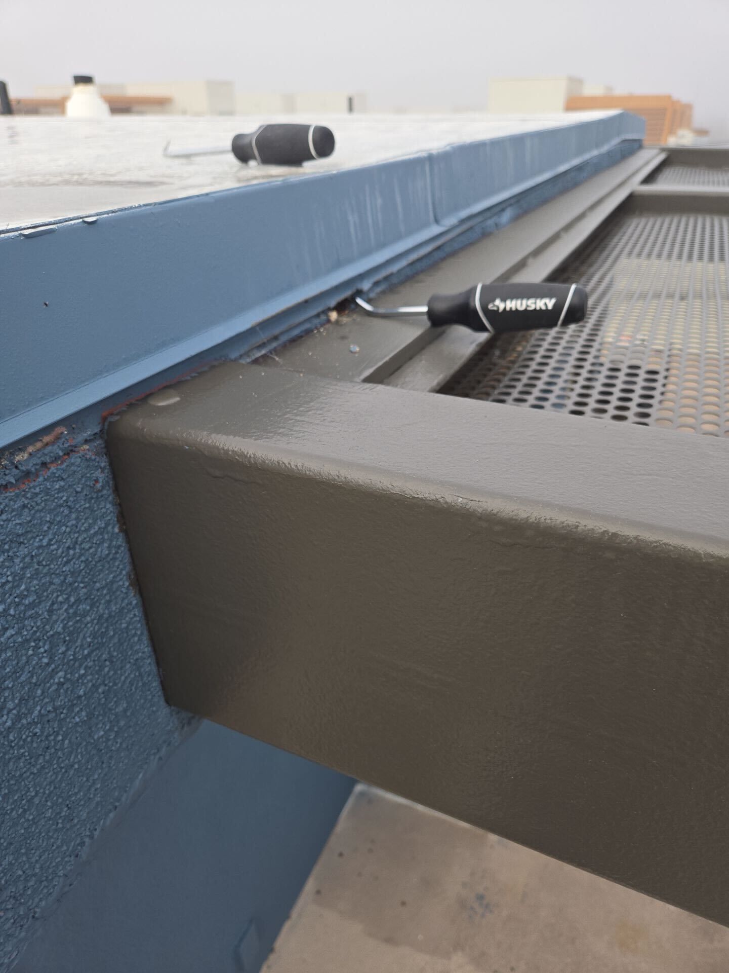 Close-up of a rooftop structure with a blue wall, gray metal framing, and a screwdriver resting on the edge.
