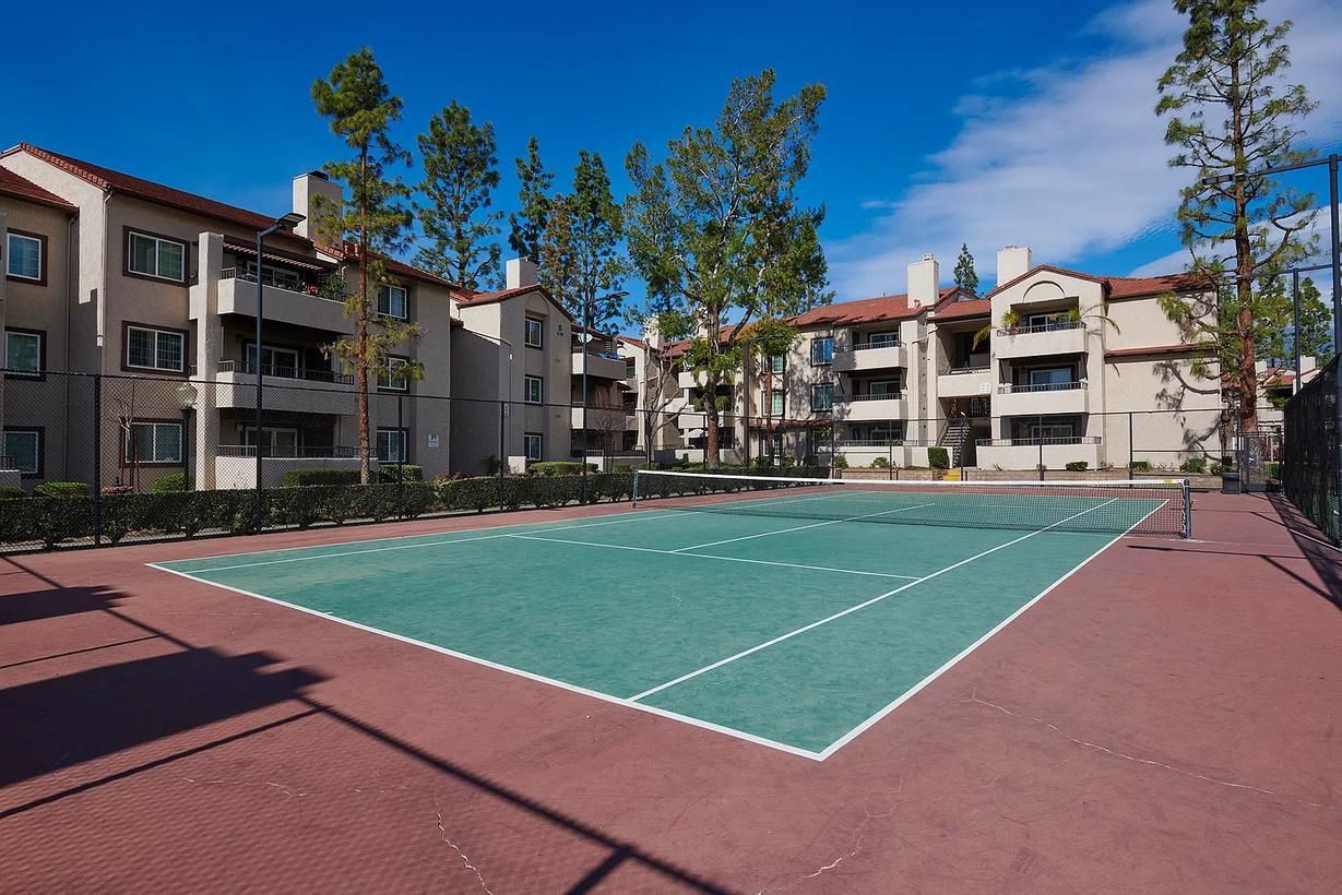 Tennis court in front of multi-story apartment buildings under a blue sky.