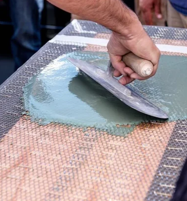 Hand smoothing green material with a trowel on a textured surface.