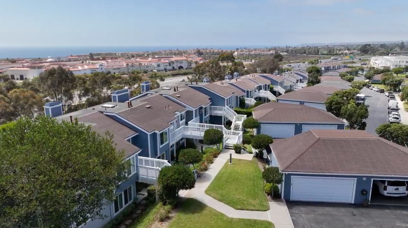 Aerial view of blue row houses with brown roofs, near the ocean, under a blue sky.
