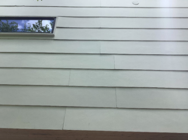 Off-white siding on a building with a small rectangular window showing a reflection of trees.