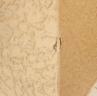 Beige stucco wall with corner damage; showing chipped paint and a vertical crack.