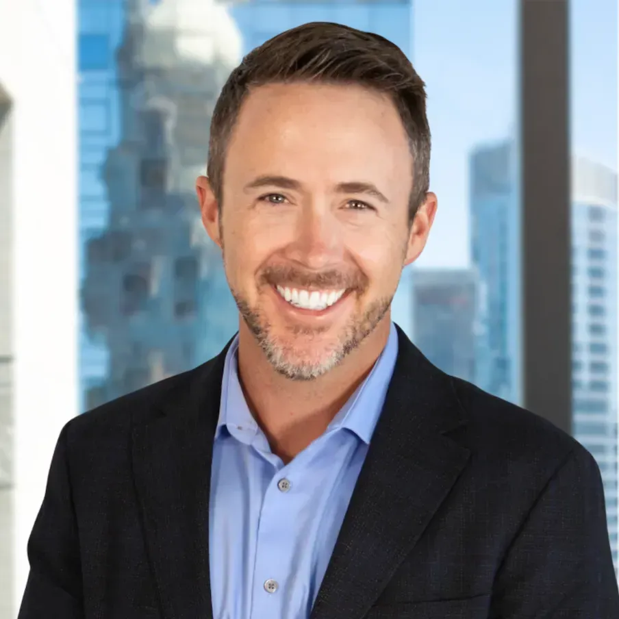 Man in blue shirt and blazer smiles widely against a city backdrop.