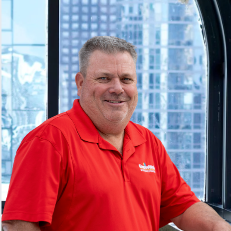 A man in a red shirt is smiling in front of a window
