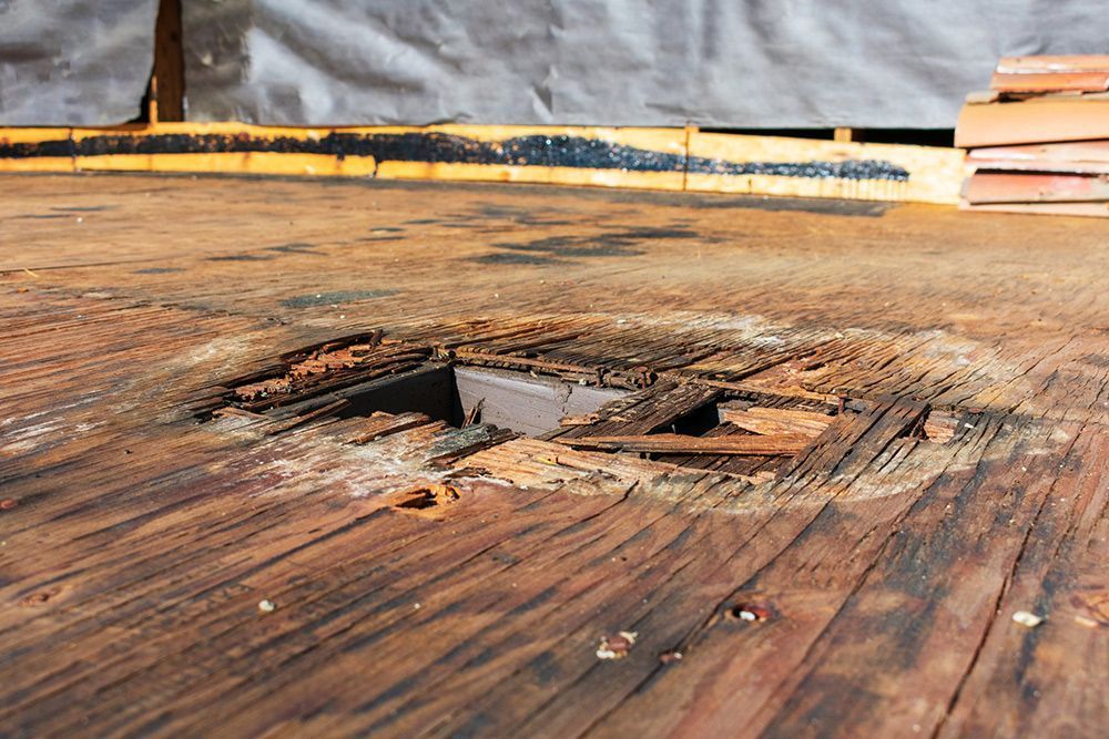 Close-up of a damaged wooden surface with a rectangular hole and splintered edges.
