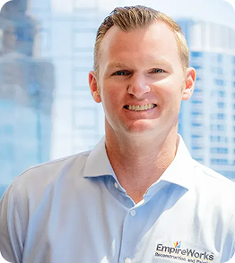 Man in light blue shirt smiling, with city skyline in the background.