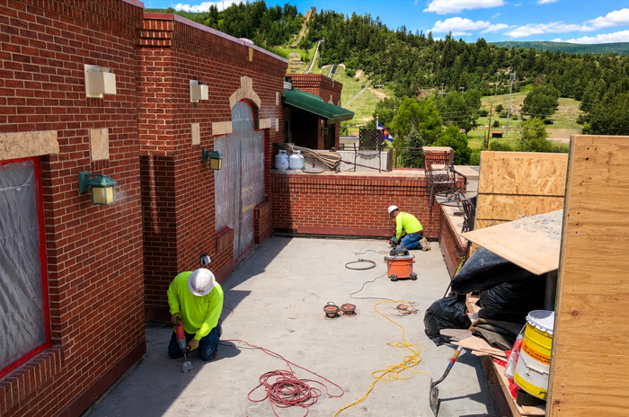 Workers in neon vests repair a brick patio beside a house, with tools and cords on the ground.