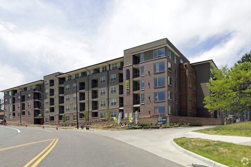 Multi-story apartment building with brick and gray siding on a sunny day.