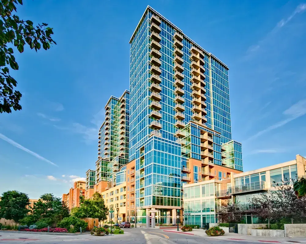 Modern high-rise apartment building with blue glass exterior against a clear blue sky.