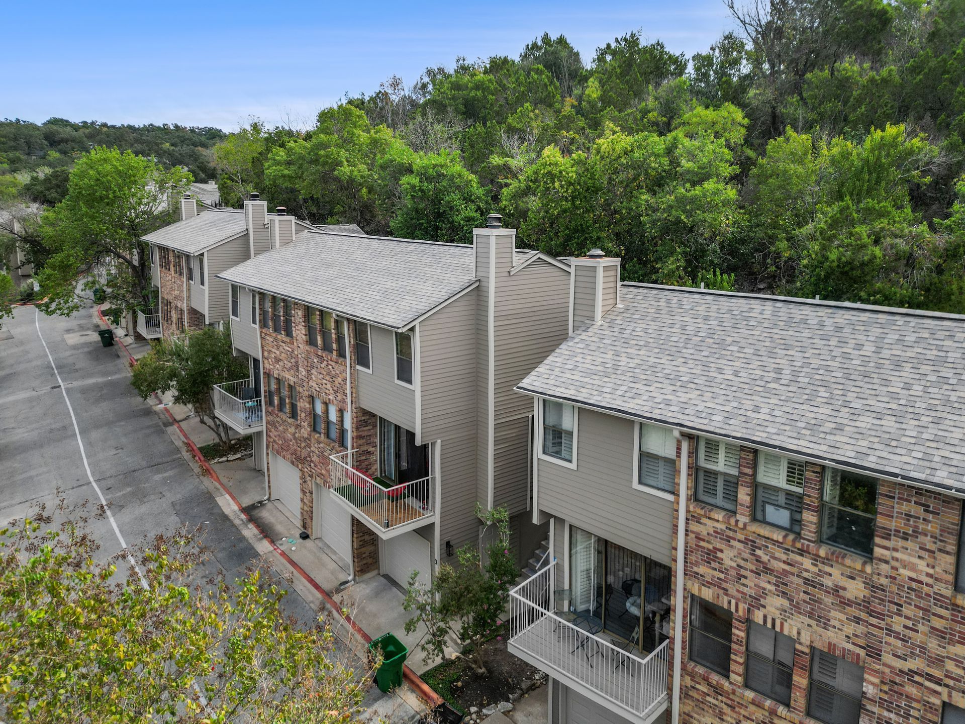 Row of multi-story townhouses with brick and siding, street in front, trees in the background.