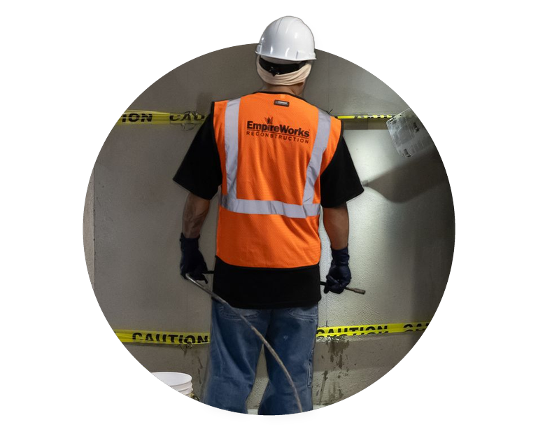 Worker in orange safety vest and hard hat inspecting a tunnel behind caution tape.