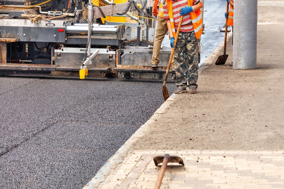 Road workers paving a sidewalk; asphalt, orange safety vests, and tools.
