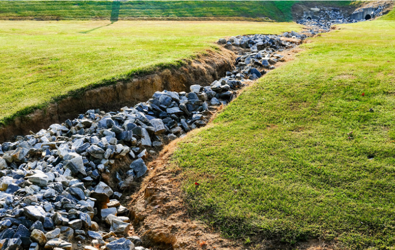 Gravel-filled drainage ditch running through grassy lawn.