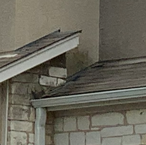 Corner of a building with stone and tan siding, roof and gutter.