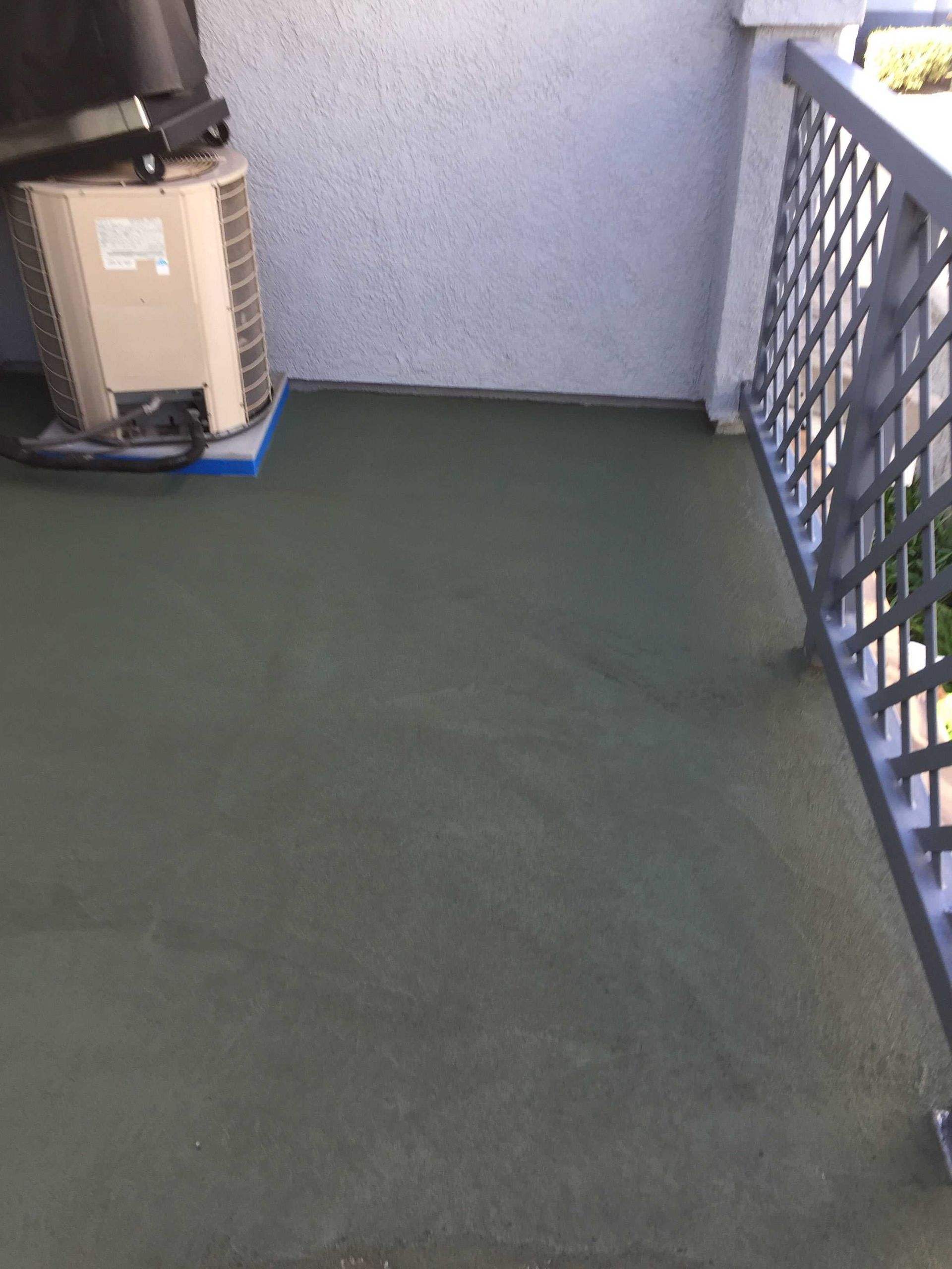 A small outdoor patio with a gray floor and railing, an AC unit is on the left.