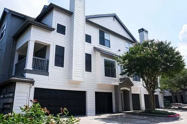 White and gray multi-story apartment building with black garage doors. Tree in front.