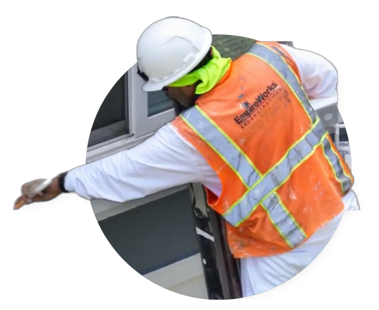 Worker in hard hat and orange safety vest reaching into a window opening
