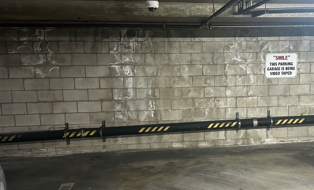 Concrete block wall in a parking garage with water stains. Black pipe with yellow stripes below