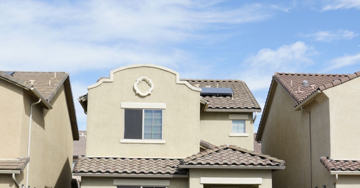Row of beige stucco townhouses with tiled roofs under a blue sky