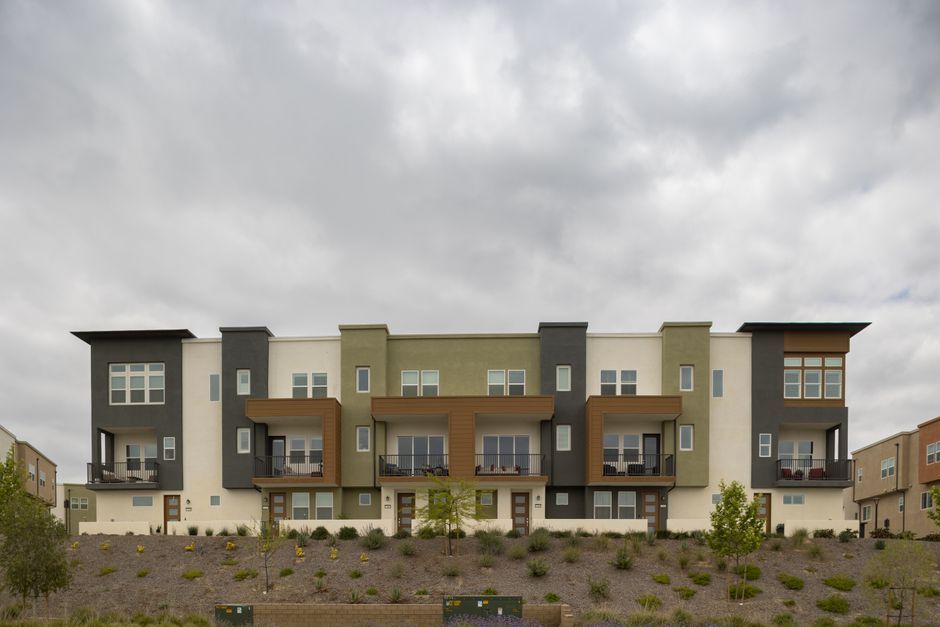 Modern multi-story apartment building with balconies under a cloudy sky, viewed from a landscaped front area