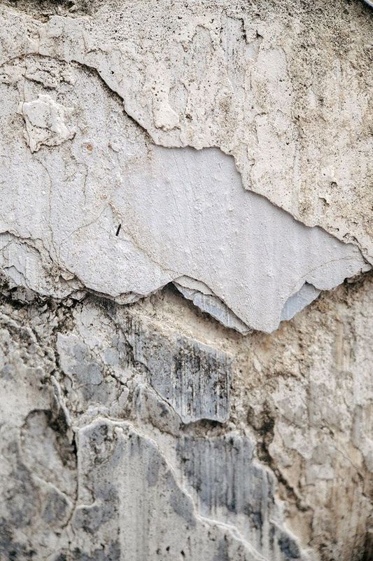 Cracked and weathered wall with peeling layers of gray and white plaster.