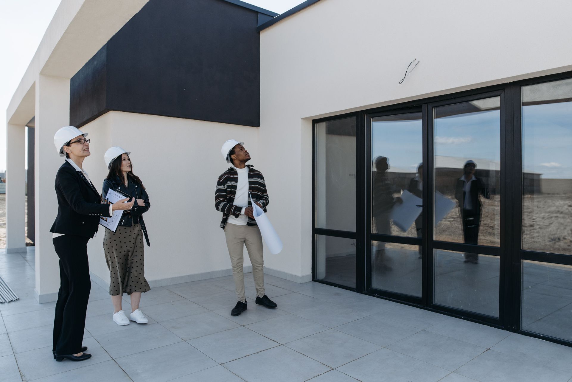 Three people stand outside a modern building, looking toward a glass entrance.