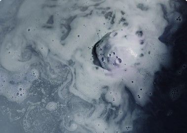 White bath water swirling with foamy bubbles surrounding a dark bath bomb.
