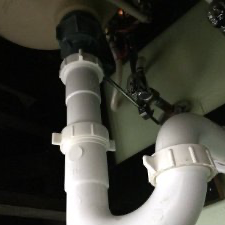 White plastic sink plumbing with visible P-trap and drain connection under a sink.