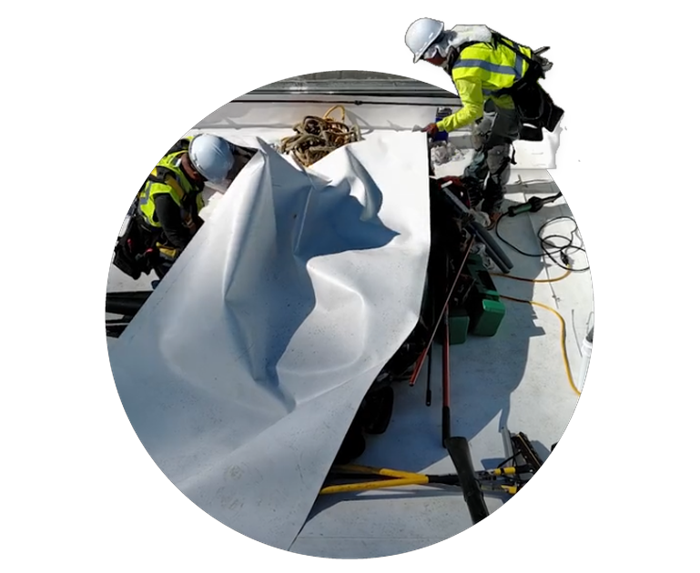 Workers inspecting damaged rooftop with a large torn white sheet and tools in bright daylight