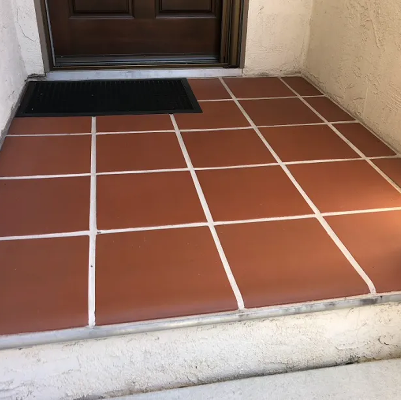 A brown tiled floor with white lines and a black mat
