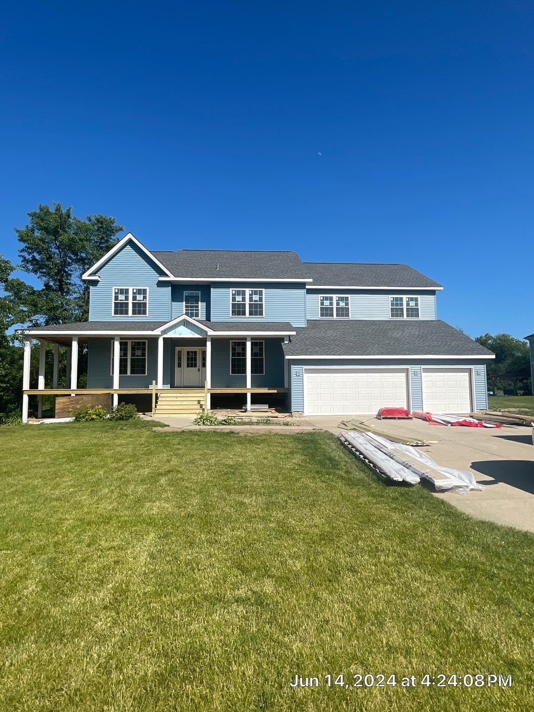 A large blue house with a gray roof is sitting on top of a lush green field.