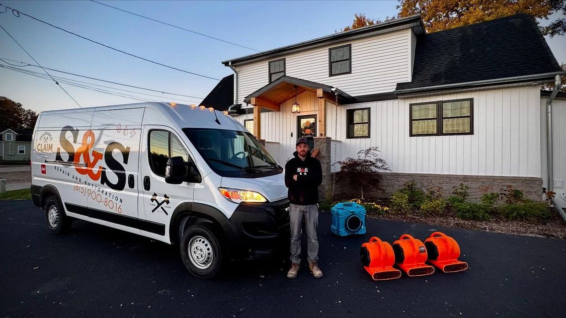 A man is standing in front of a van in front of a house.