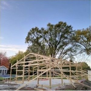 A wooden structure is being built in a field with trees in the background.