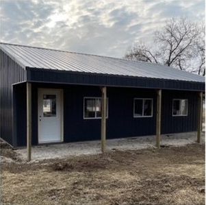 A black metal building with a white door and windows is sitting in the middle of a field.