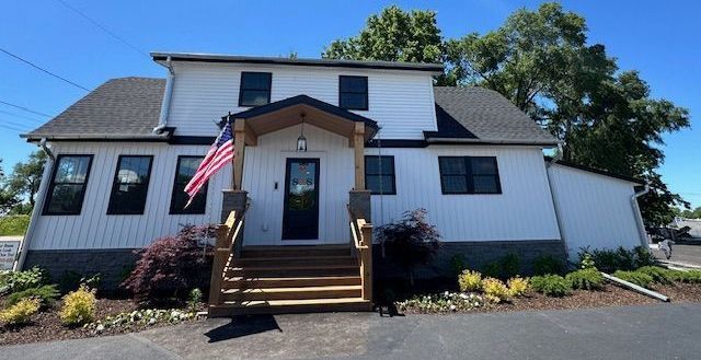 A white house with a black roof and an american flag on the front porch.