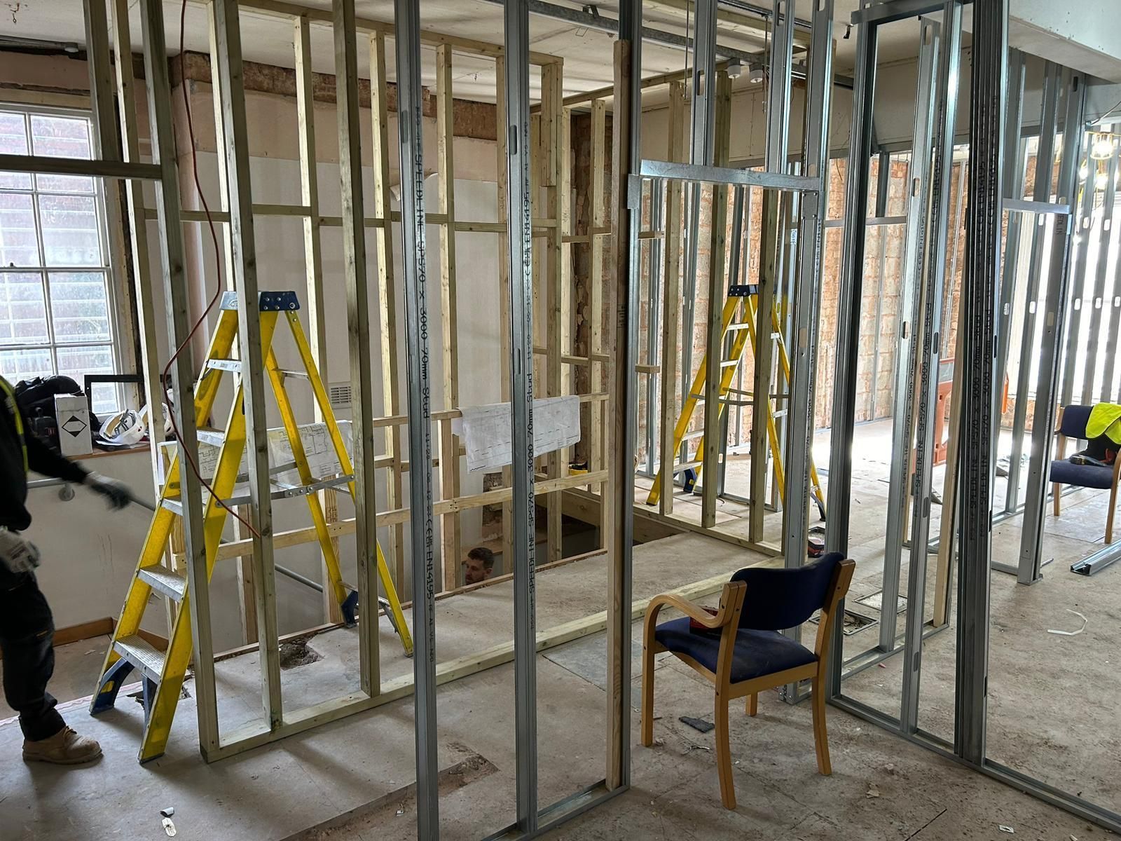 A man is standing in a room with a ladder and chairs.