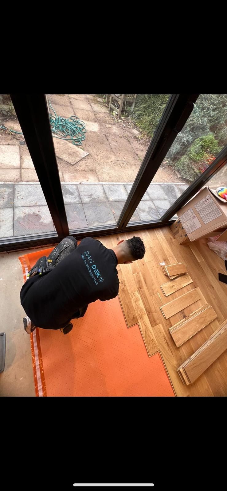 A man is kneeling on a rug in front of a large window.