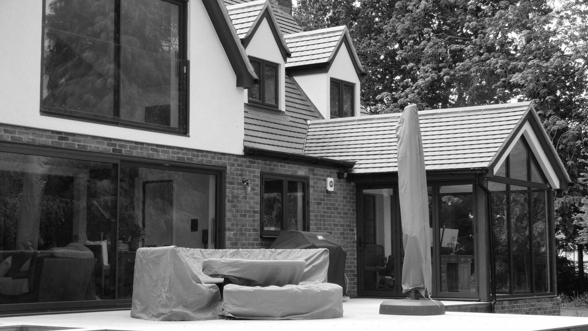 A black and white photo of a house with a patio and umbrella.