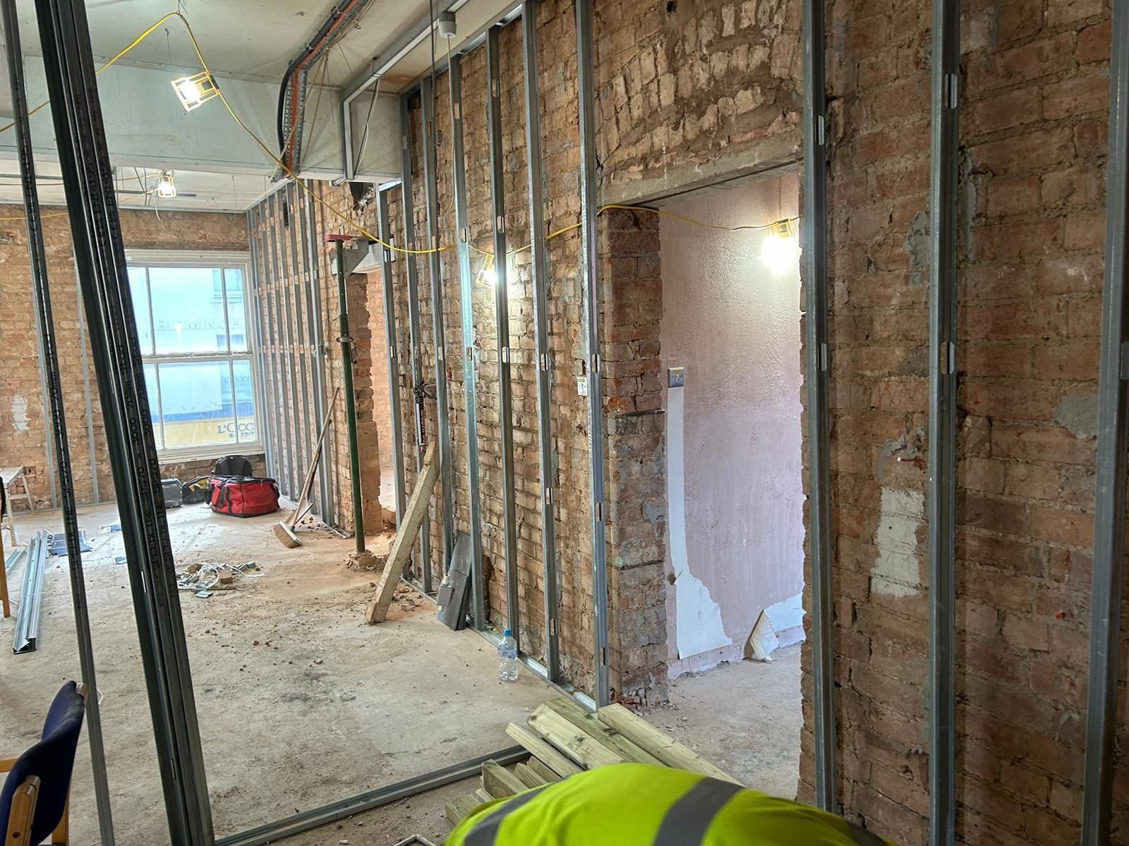 A man in a yellow vest is laying on the floor in a room under construction.