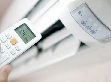 A person is holding a remote control in front of an air conditioner.