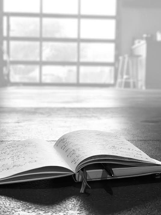 A black and white photo of an open book on a wooden table.