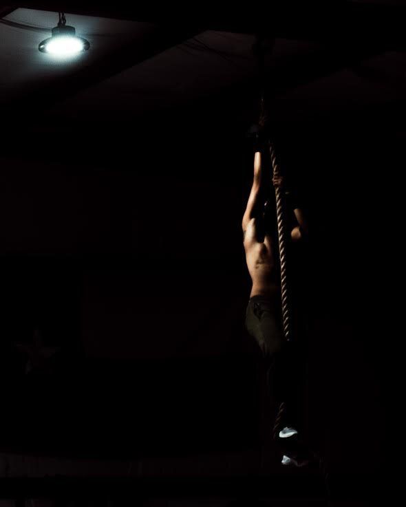 A man is climbing a rope in the dark.