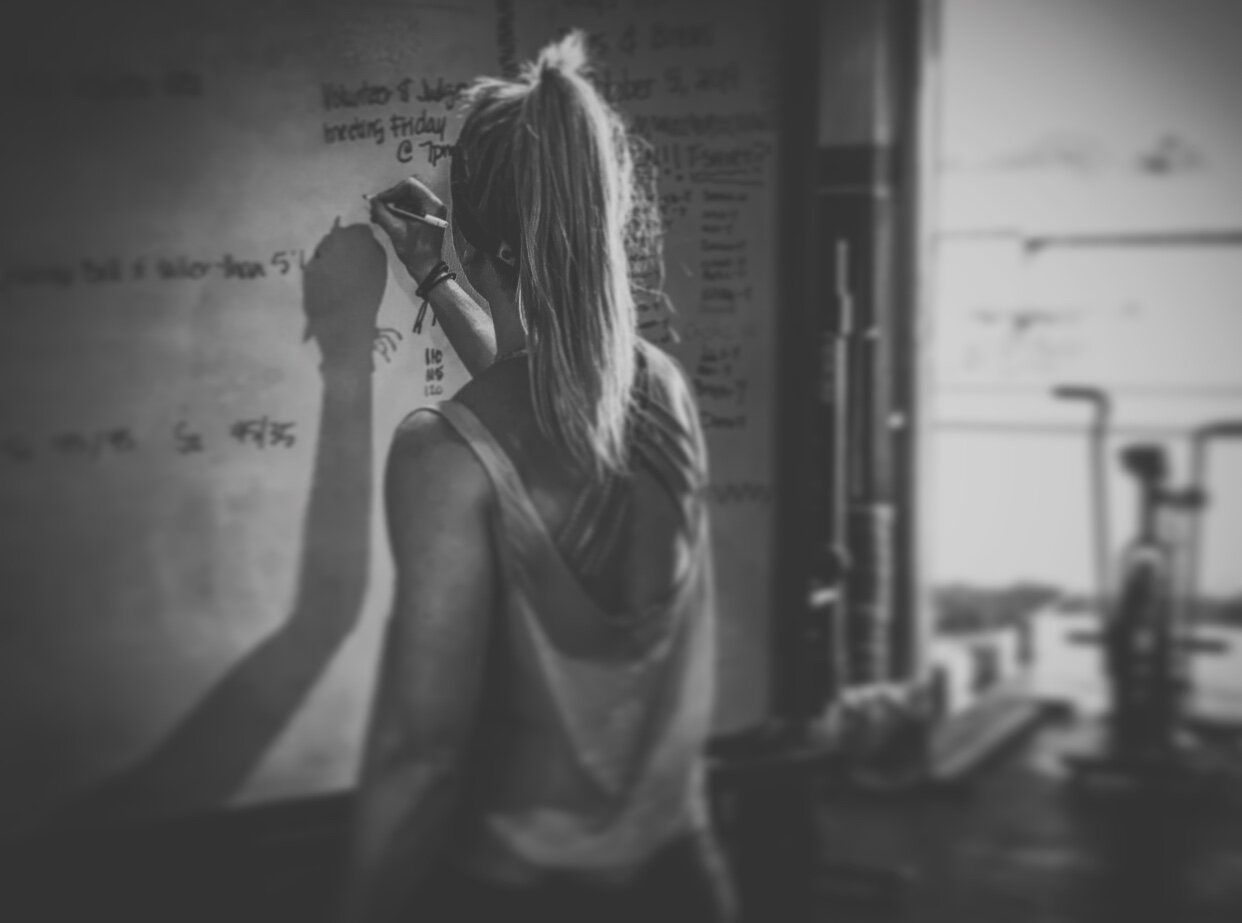 A woman is writing on a whiteboard in a gym.