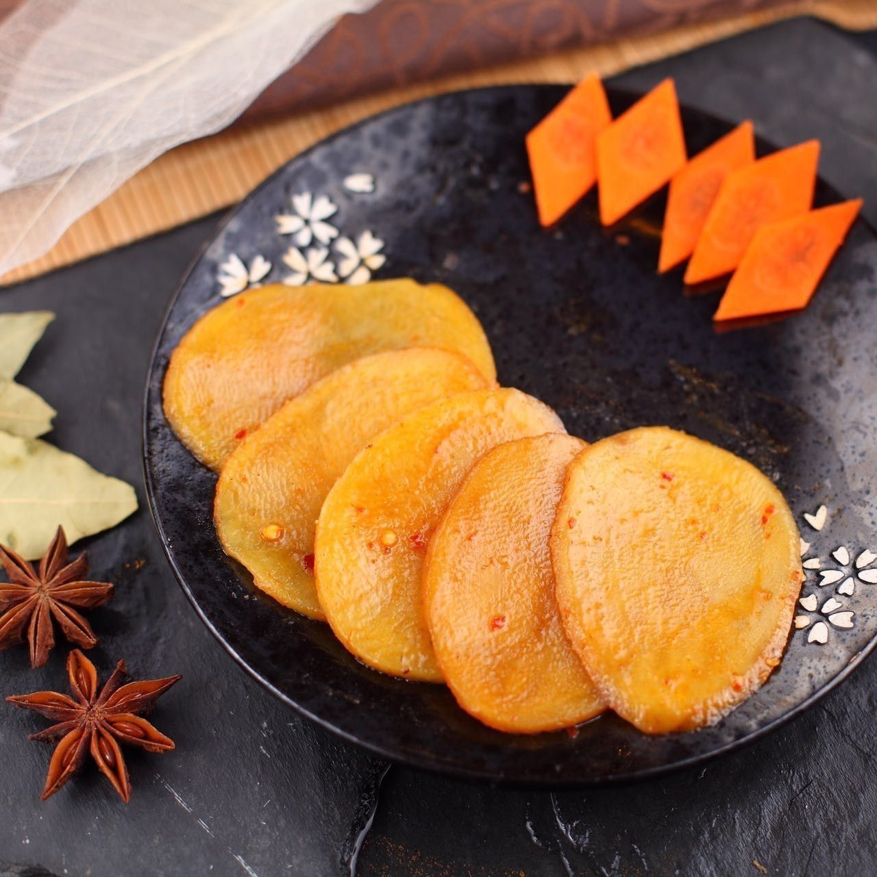 Golden fried snacks on a black plate with star anise and orange garnish on a dark tabletop