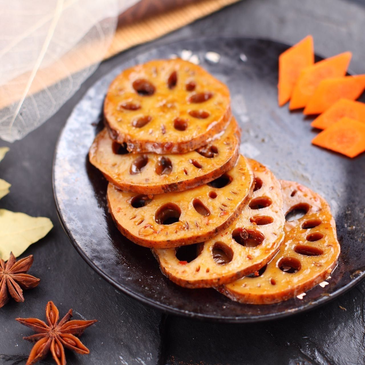 Sliced lotus root chips on a dark plate with star anise and orange garnish