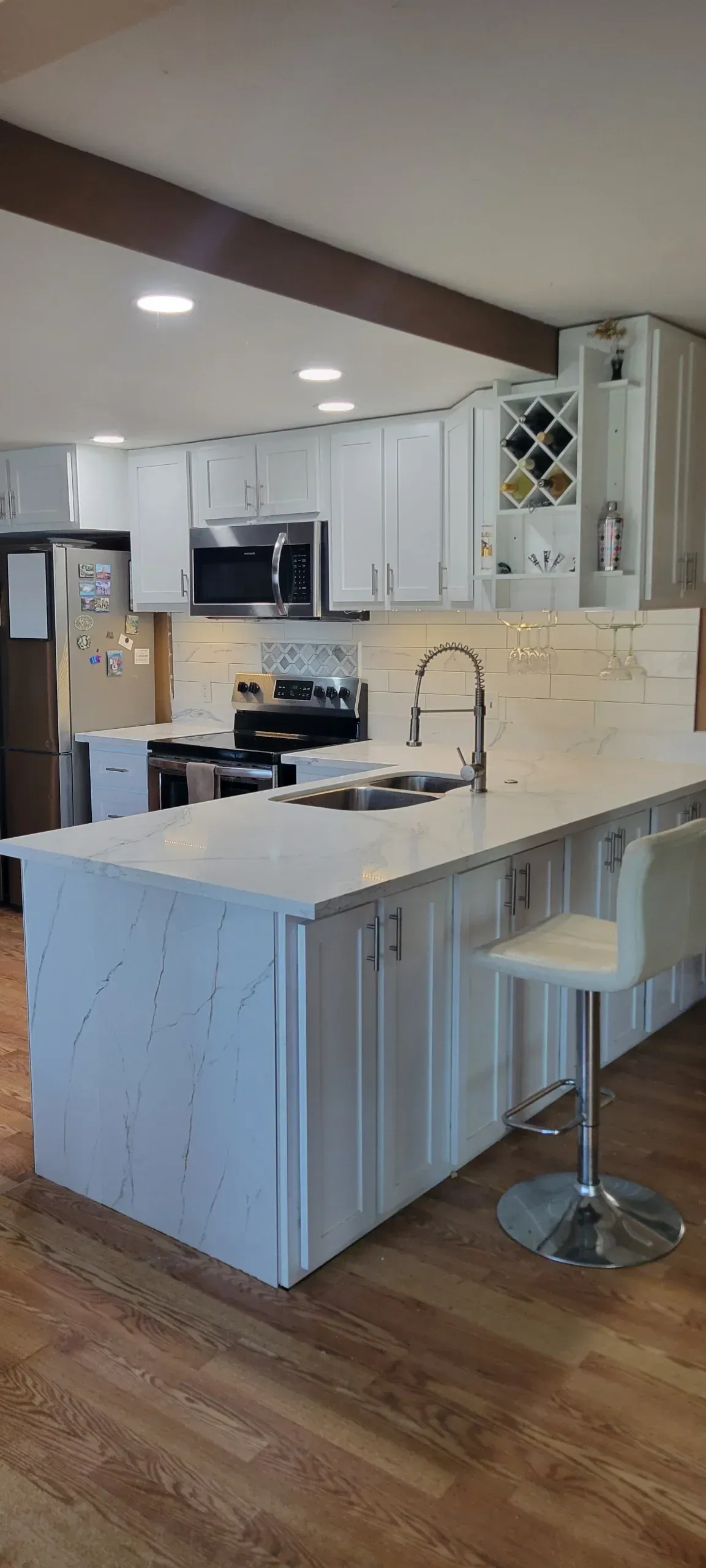 A kitchen with white cabinets , stainless steel appliances , a sink , and a large island.