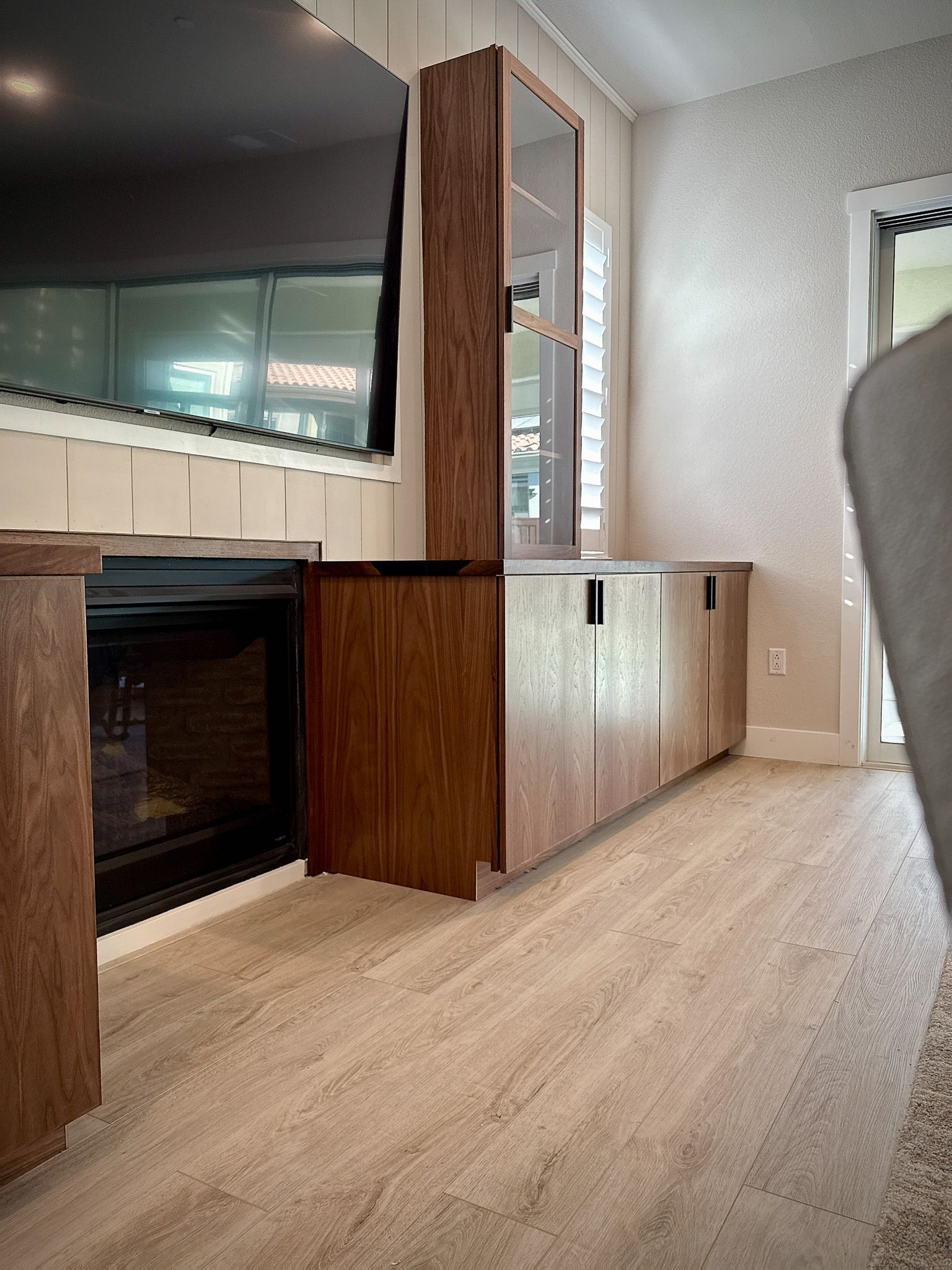 Wooden media center with tall cabinet, built-in fireplace, and TV on a light wooden floor.