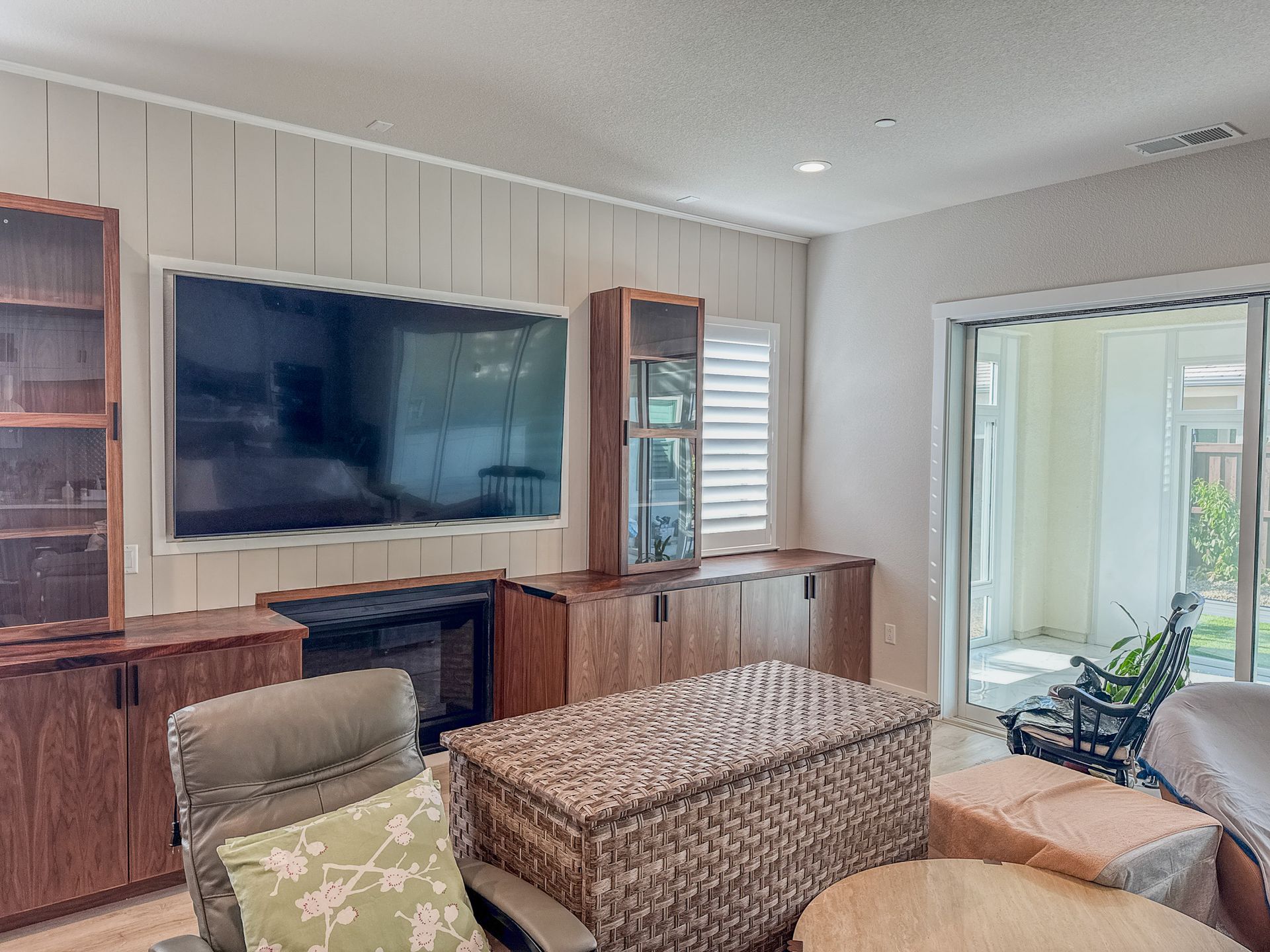 Living room with large TV, wooden cabinets, and a view to a patio.